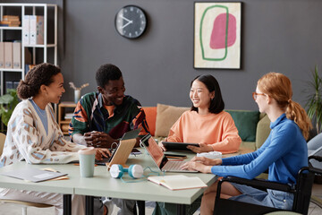 Diverse group of young people laughing happily while enjoying work together during meeting in IT office