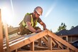 © Stavros - A male roofer is in the process of strengthening the wooden structures of the roof of a house. A middle-aged Caucasian man in hardhat is working on the construction of a wooden frame house.
