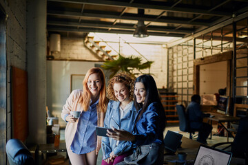 Wall Mural - Young and diverse group of female designers taking a selfie on a smartphone while working in a startup company office