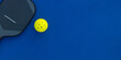 © Mike Orlov - Pickleball tennis racket on the court. Blue background with copy space. Sport court and ball.