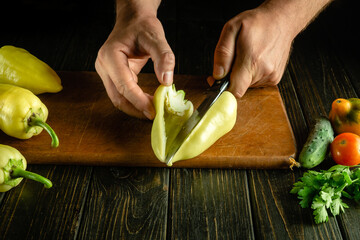 Peeling peppers with a knife in the hands of a cook on the kitchen table. Concept of preparing a vegetable dish for lunch