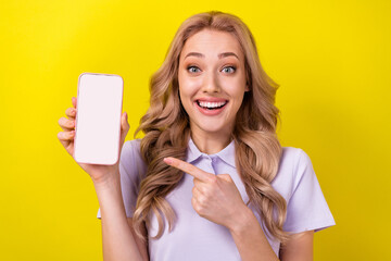 Poster - Portrait of charming impressed girl direct finger arm hold show empty space smart phone display isolated on yellow color background