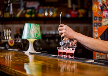 Red alcoholic drink in glasses on bar. Red cocktail at the nightclub. Barman preparing cocktail shooter. Bartender pouring strong alcoholic drink into small glasses on bar. Shots at the nightclub