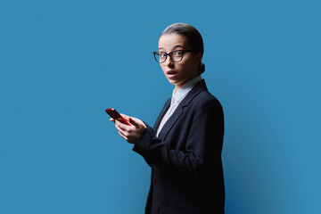 Surprised shocked teenage female with smartphone on blue studio background