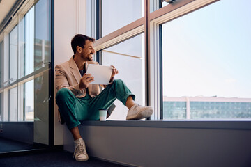 Wall Mural - Happy entrepreneur using digital tablet while looking through window in office.