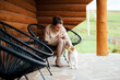Smiling woman petting cat while sitting near wooden house