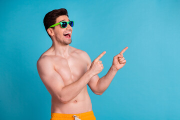 Wall Mural - Photo portrait of attractive young man finger point look empty space dressed stylish yellow shorts isolated on blue color background