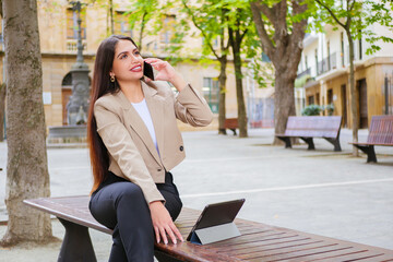 Multitasking Business woman work on park of city talking phone in happy mood smiling. Portable Productivity whit mobile office.