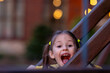 Happy little girl looking at camera with open with joy mouth, standing behind fence from construction on playground.
