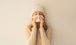 Sick upset woman sneezing blow nose using tissue wearing warm soft knitted clothes, hat and sweater on beige studio background