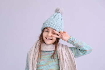 Wall Mural - Cute little girl in winter clothes showing victory gesture on lilac background, closeup