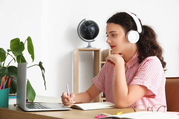 Wall Mural - Female student in headphones with laptop doing lessons at home