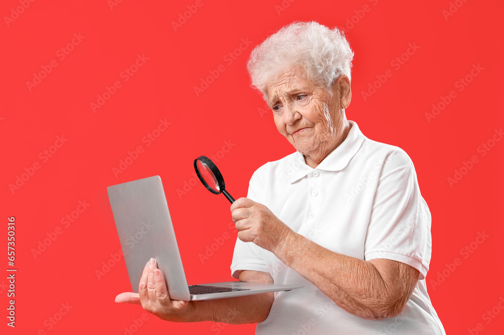 Senior woman with magnifier and laptop on red background