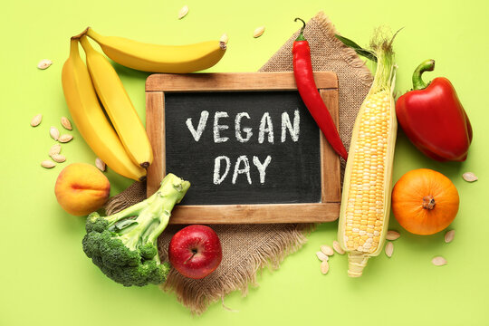 Board with text VEGAN DAY, fresh vegetables and fruits on green background