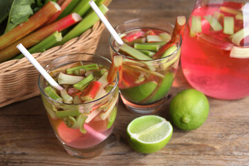 Glasses and jug of tasty rhubarb cocktail with lime fruits on wooden table