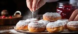 Fototapeta  - Female makes homemade jam filled donuts cooking Jewish Hanukkah treats sprinkling powdered sugar on Berliners With copyspace for text