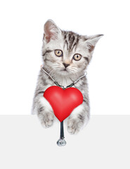 Sticker - Tabby kitten with stethoscope on his neck looks above empty white banner and holds red heart. isolated on white background