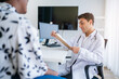 © kelvn - Male doctor in white medical uniform consult female patient on consultation. They Consult Digital Tablet Computer while Talking about Patient's Health.