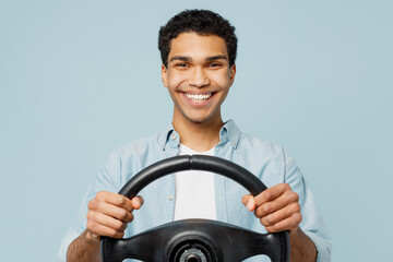 Wall Mural - Young smiling cheerful fun cool man of African American ethnicity he wearing shirt casual clothes hold steering wheel driving car isolated on plain pastel light blue cyan background studio portrait.