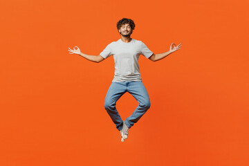 Wall Mural - Full body young Indian man he wear t-shirt casual clothes jump high hold spreading hands in yoga om aum gesture relax meditate try to calm down isolated on orange red color background studio portrait