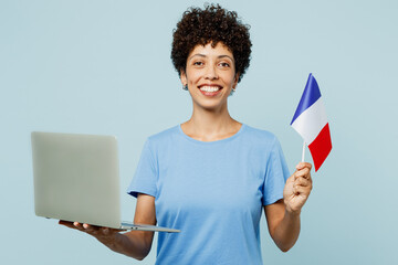 Wall Mural - Young IT woman of African American ethnicity wear t-shirt casual clothes hold in hand French flag use work on laptop pc computer isolated on plain pastel light blue cyan background. Lifestyle concept.