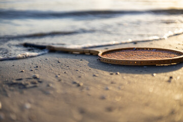 badminton racket on the sand in water at sunset