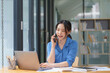 © Songsak C - Beautiful businesswoman using a smartphone and working with a laptop while sitting at an office desk, working from home concept.