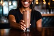 hand serving a frothy chocolate milkshake with a broad smile