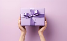 Female Hands Holding A Purple Gift Box With A Bow Against Pastel Background.