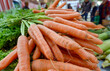 Einkaufen auf dem Wochenmarkt: Blick auf eine Auswahl an knackigen Karotten und Bundmöhren an einem Verkaufsstand draußen mit Menschen im verschwommenen Hintergrund, selektiver Fokus, Copyspace