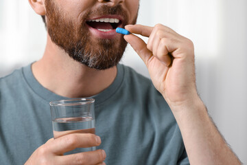 Canvas Print - Man with glass of water taking pill on blurred background, closeup