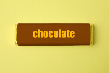 One chocolate bar in packaging on yellow background, top view