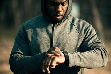 Wall Mural - Young man checking his smartwatch before doing a workout in a outdoor park