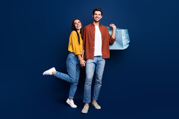 Aufkleber - Full length portrait of cheerful funny partners hold hands carry store bags isolated on blue color background
