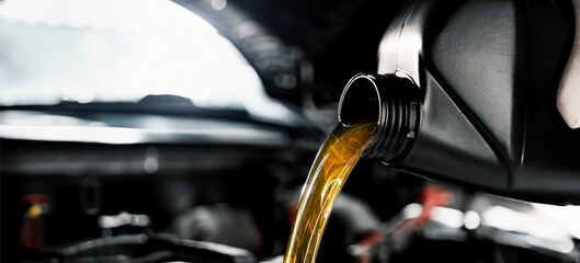 mechanic pouring motor oil from bottle into engine at car repair shop. banner with copy space