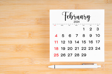 February 2024 calendar page and pen on wooden background.