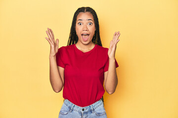 Young Indonesian woman on yellow studio backdrop celebrating a victory or success, he is surprised and shocked.