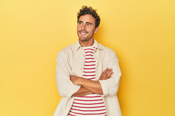 Wall Mural - Young Latino man posing on yellow background smiling confident with crossed arms.