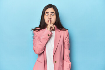 Young Caucasian woman on blue backdrop keeping a secret or asking for silence.