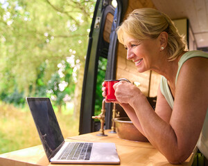 Wall Mural - Senior Woman On Camping Trip In Countryside Working Inside RV Using Laptop