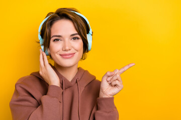 Poster - Portrait of young charming woman wear brown sweatshirt listen wireless earphones point finger mockup spotify isolated on yellow background