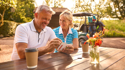 Wall Mural - Senior Couple Sitting Having Coffee After Round Of Golf Looking At Score Card Together