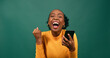 © Meeko Media - Young Black woman reads text message shocked excited, green studio background