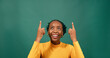 © Meeko Media - Beautiful Black woman pointing up at copy space, green studio background