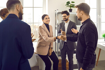 Wall Mural - Team of business people congratulating young woman on her success. Happy young woman smiles and shakes hands with man while colleagues are applauding. Recognition at work concept