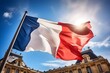 A stunning French national tricolor flag flies in the wind on a flagpole with traditional French buildings in the background. Natural daylight. 