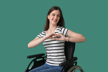 Wall Mural - Young woman making heart gesture in wheelchair on green background