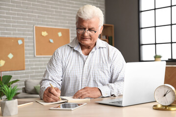 Canvas Print - Senior man with laptop writing in notebook at home