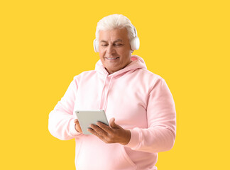 Canvas Print - Senior man in headphones using tablet computer on yellow background