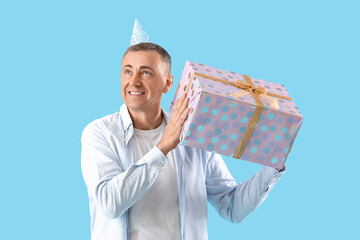 Poster - Mature man in party hat with birthday gift on blue background